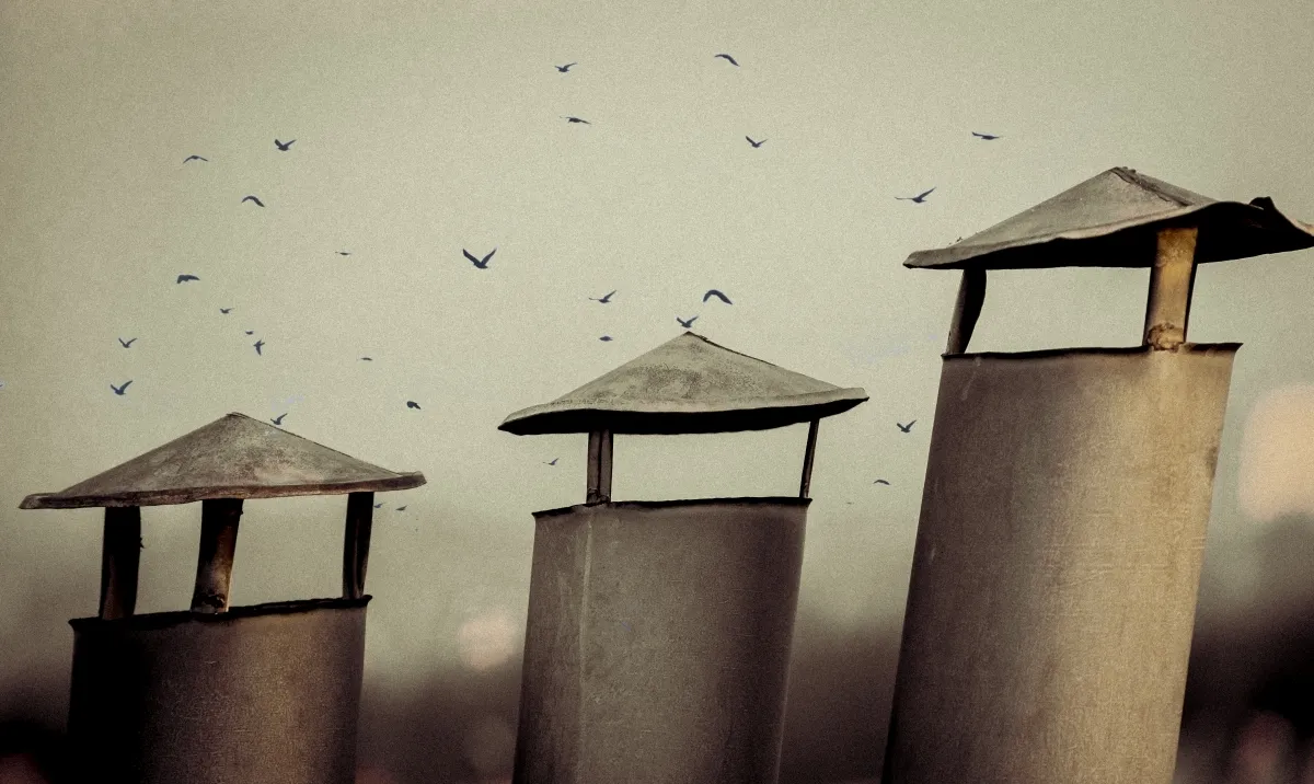 Three metal chimneys with birds flying in the background